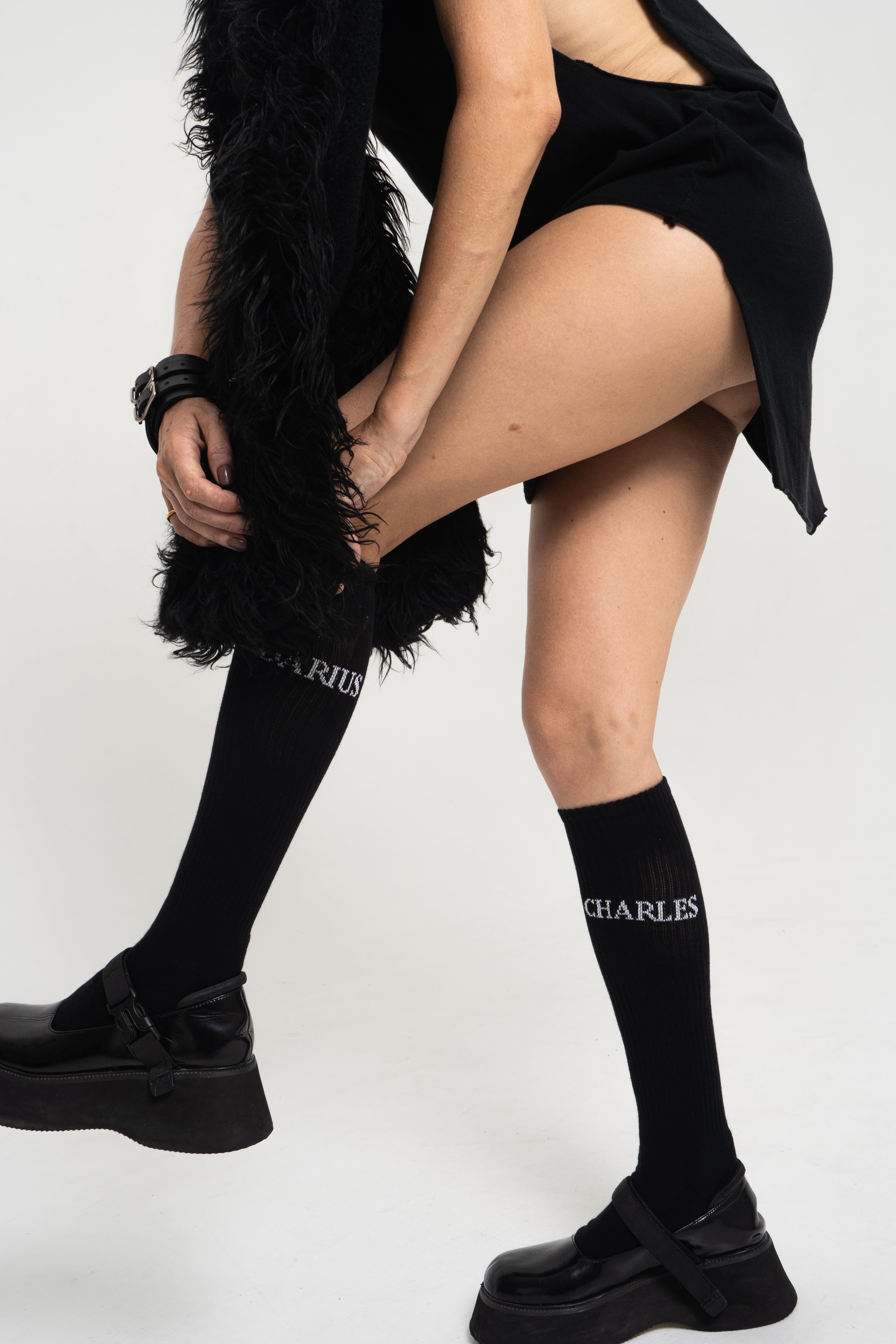 Female model adjusting pose while wearing black Charles Darius High Socks – luxury Japanese cotton knee-highs styled with black platform shoes.