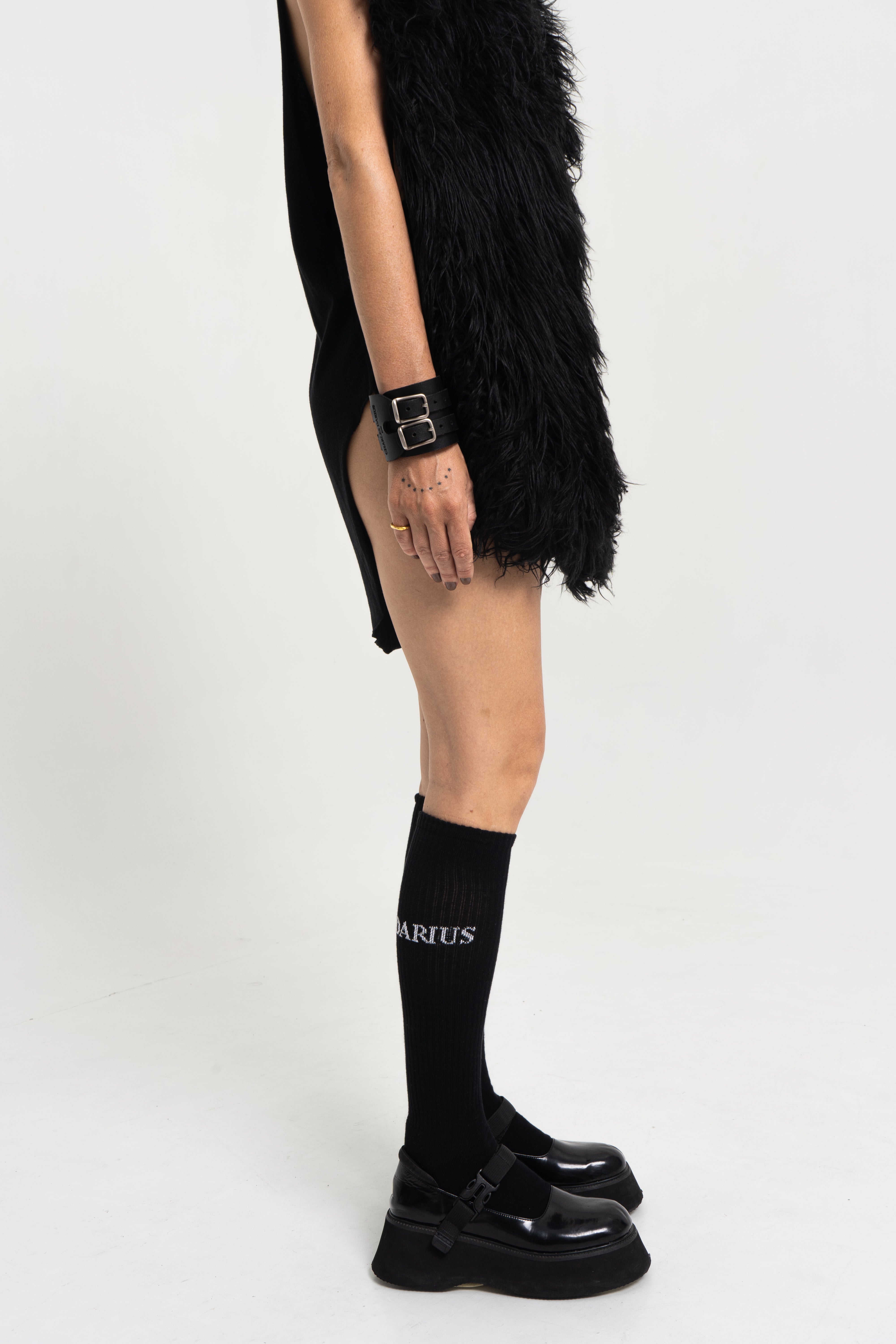 Female model side profile wearing Charles Darius High Socks in black with logo detailing, paired with black Mary Jane shoes.