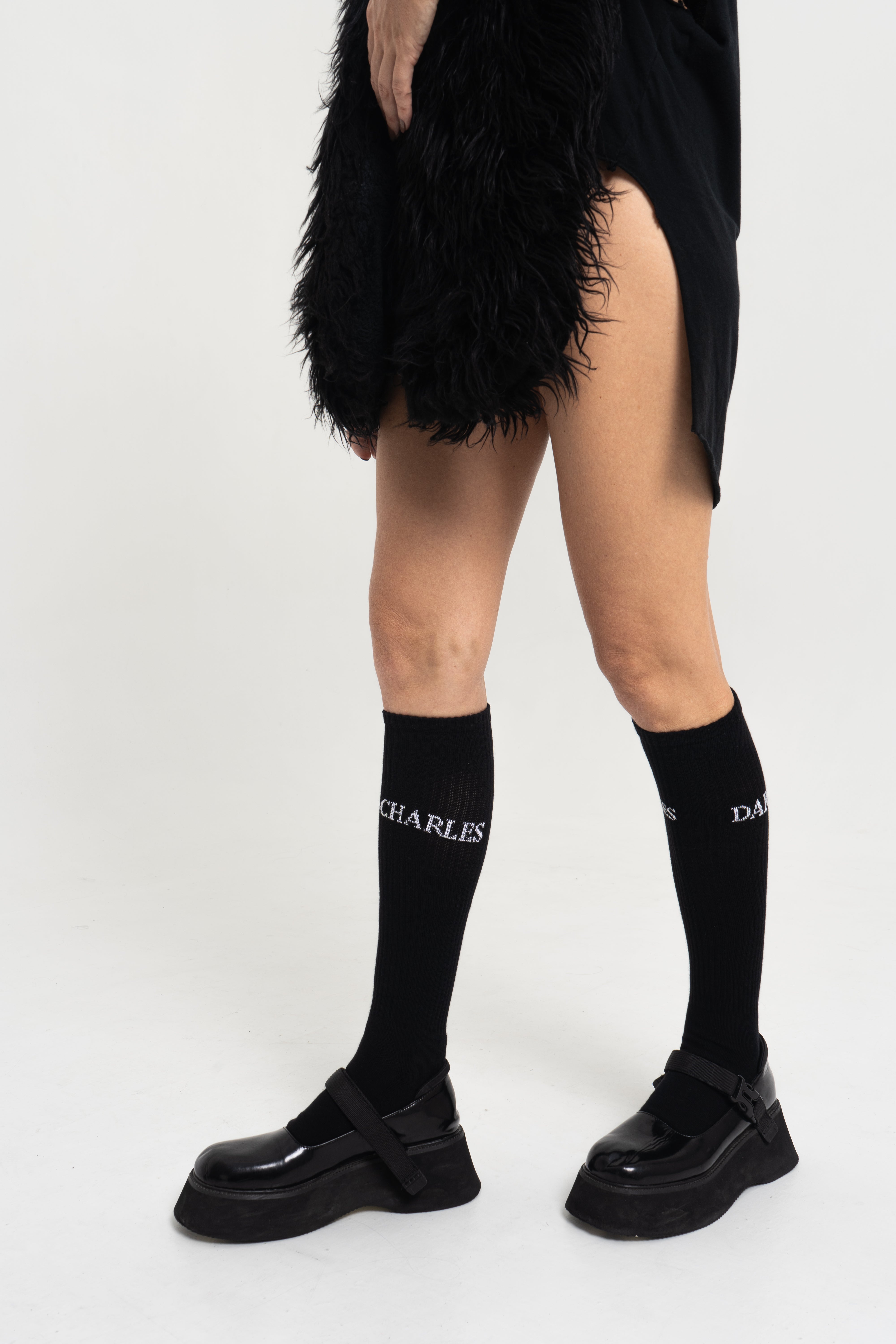 Black Charles Darius High Socks with woven logo, styled on model with platform shoes, side profile studio shot.